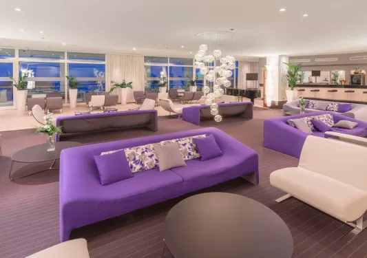 Indoor lounge with white and purple sofas and large windows in the background