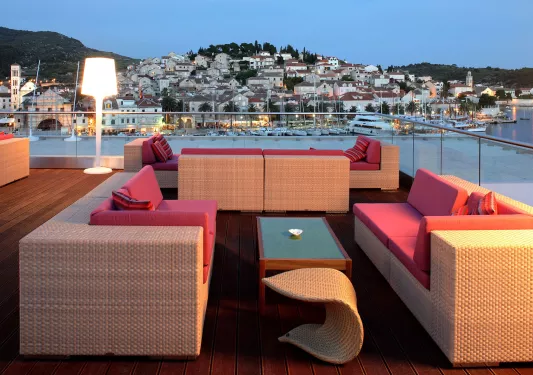 Outdoor balcony with woven sofas with cushioned pillows, looking out to a small town