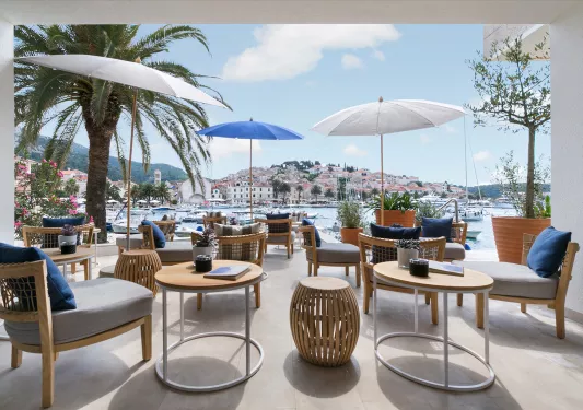 Outdoor patio with gray, cushioned chairs, gray and blue umbrellas looking out towards the ocean