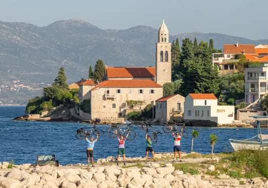 Group of people holding bikes over their heads, with a town and ocean in the background