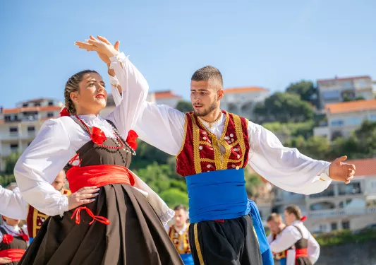 Man and woman wearing traditional attire, dancing with a group of other people