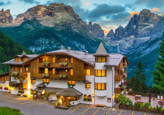Exterior of white and brown hotel building, with large mountains in the background