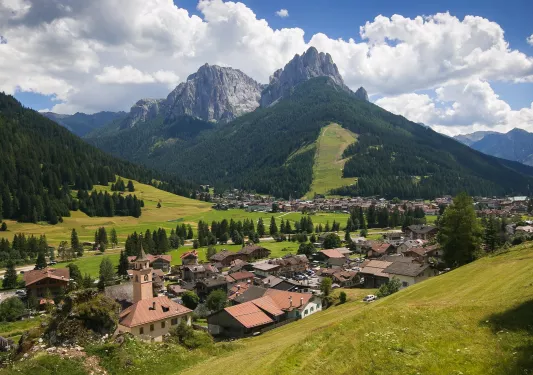 Valley of grass with tall mountains and brown houses on the ground level