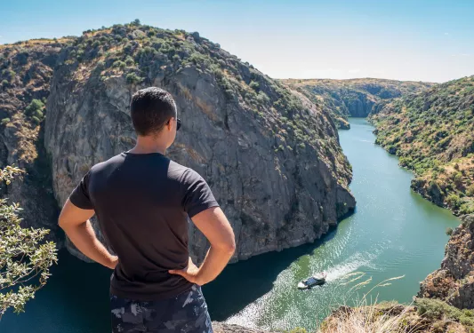 Man standing on a cliff looking down at a river