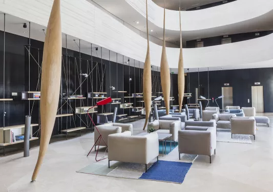 Indoor building lobby and seating area with white, cushioned chairs with large wooden sculptures