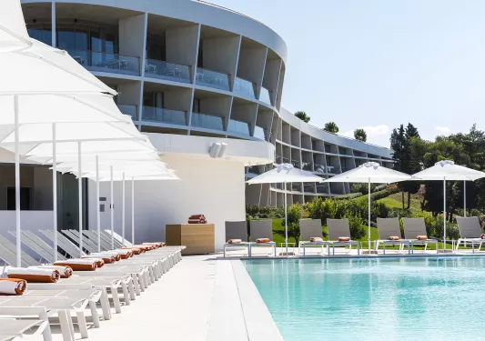 Outdoor pool, with white umbrellas and chairs surrounding the pool and a building in the background