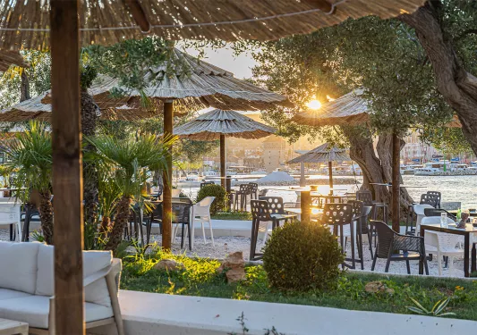 Straw umbrellas over chairs and tables, with views of the beach in the background