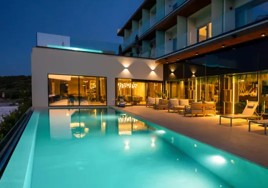 Outdoor pool illuminated in the nighttime, with a large hotel building to the right
