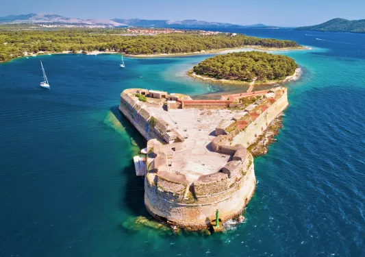Stone, rustic building in the ocean, with a forest in the background
