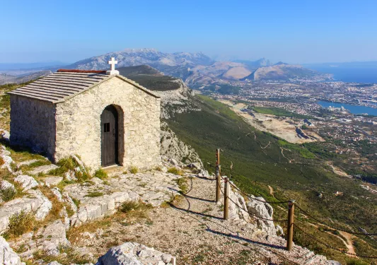 Church hut building on top of a hill, overlooking a town and grassy hills