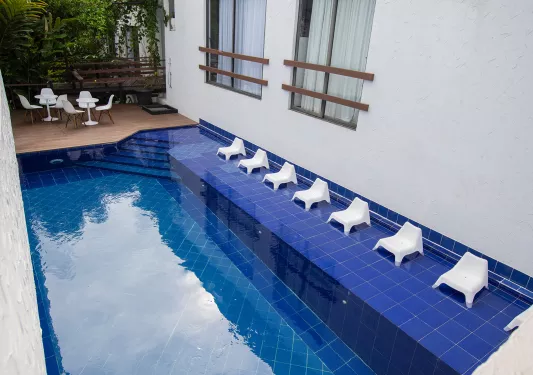 Outdoor blue pool, surrounded by white chairs and a white building to the right