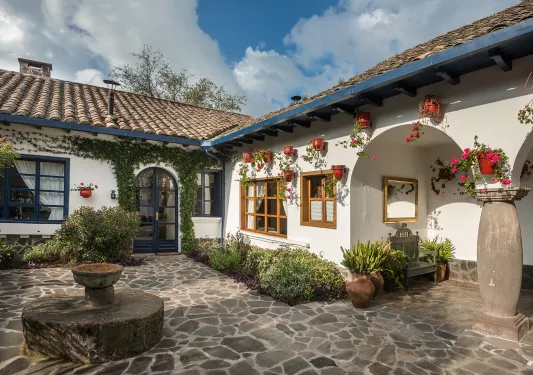 Exterior view of white building with a small fountain and stone flooring in front
