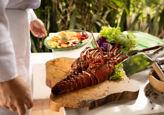 Cooked lobster on a wooden plank, with a plate of vegetables to the left