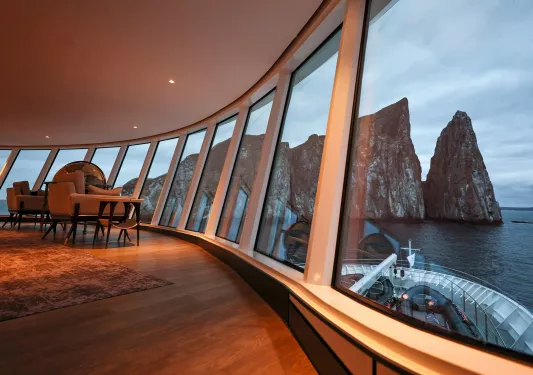 Cruise ship interior with sofas and wooden tables next to a large wall of windows