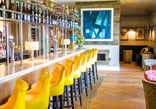 Bar and lounge with yellow bar stools and a fireplace to the right