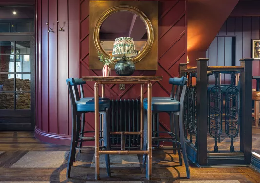 Dining table with a copper tables and blue stools, with a large mirror hanging on the wall