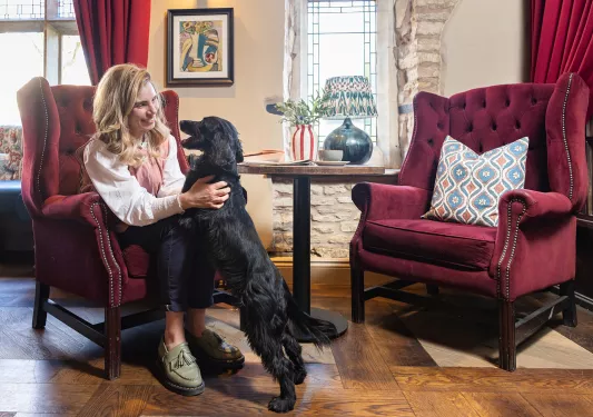 Woman sitting on a red, cushioned chair while playing with a black dog
