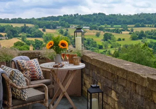 Outdoor stone balcony with cushioned chairs looking towards a grassy valley