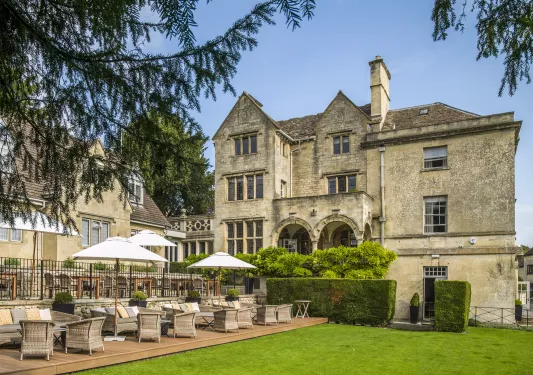 Exterior view of stone building with an outdoor patio with cushioned chairs and white umbrellas