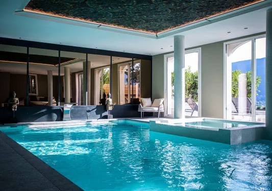 Indoor swimming pool with large mirrors and windows with views of an outdoor patio