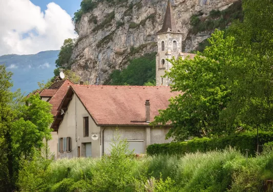 Beige stone building with a bell tower, surrounded by tall trees