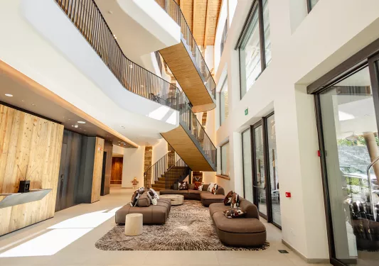 Interior view of tall hotel lobby with large staircase and brown sofas on the ground floor