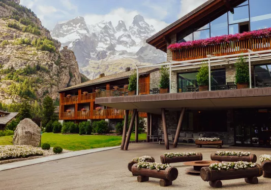 Exterior view of lodge hotel building with wooden benches in front and mountains in the background