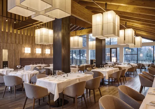 Indoor restaurant dining area with long tables with white table cloths, with cushioned gray chairs surrounding