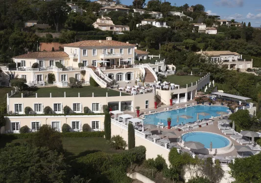 Sky, exterior view of white hotel building with an outdoor pool, surrounded by trees