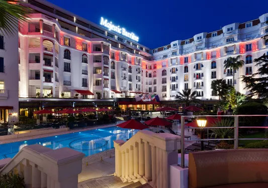 Exterior view of hotel building with an outdoor pool and red umbrellas