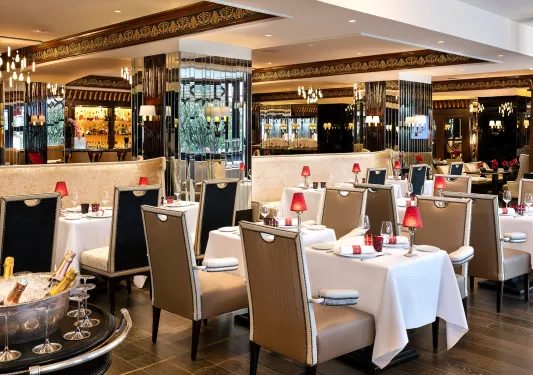 Indoor dining hall with multiple dining tables and cushioned chairs, with wine glasses on each table
