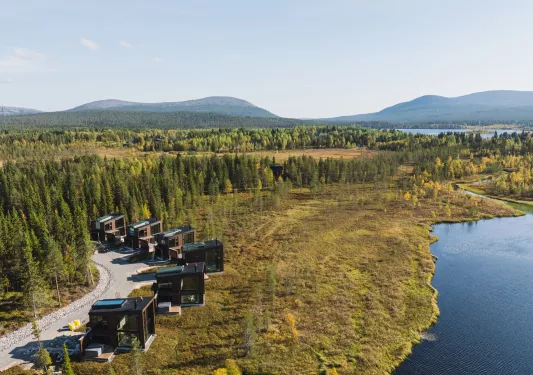 Sky view of a grassy valley with large, black cottages along a river