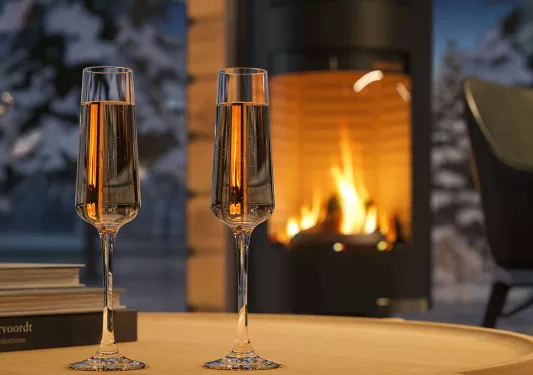 Two glasses of champagne on a table in front of a fireplace