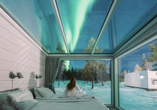 Woman sitting in a glass room looking up at the northern lights