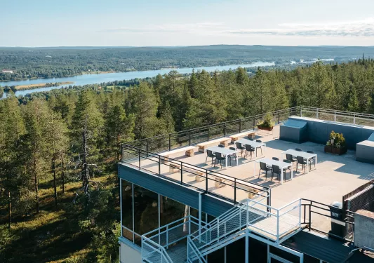 Sky view of building rooftop with chairs and tables, looking out to tall trees
