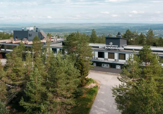 Exterior view of gray and white hotel building, with tall trees in front