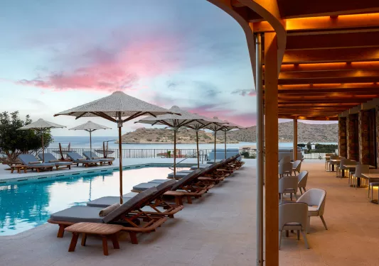Outdoor pool surrounded by reclining chairs and the ocean in the background