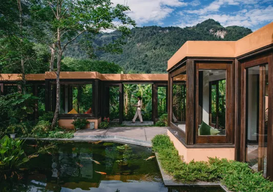 Exterior view of wooden building with large glass windows and a pond in front