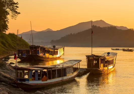 Large boats docked by the shore with the sunset in the background