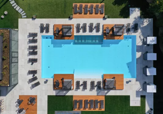 Sky view of an outdoor pool, surrounded by black chairs and wooden platforms