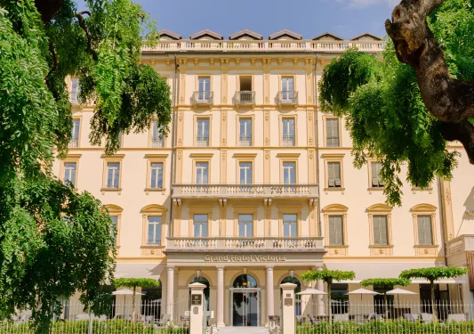 Exterior view of yellow hotel building, surrounded by tall green trees