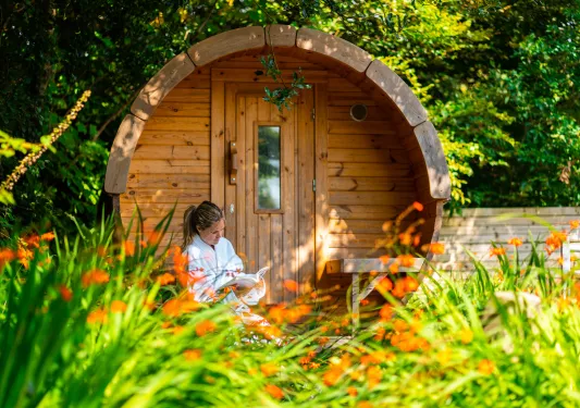 Woman sitting in front of a wooden cabin building, reading a book