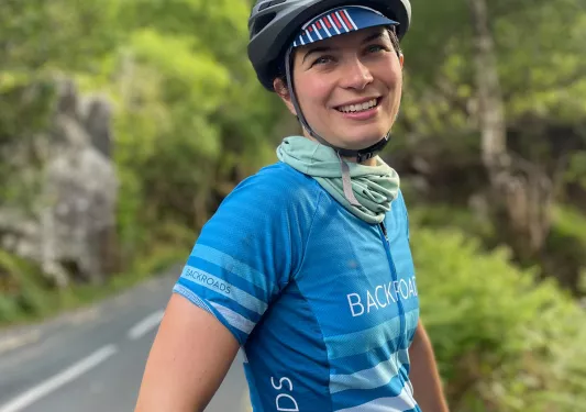 Woman wearing a Backroads jersey and helmet, with a road surrounded by trees in the background