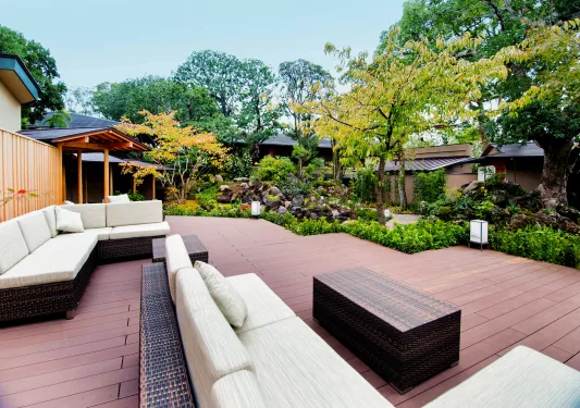 Outdoor patio with cushioned sofas, surrounded by tall green and yellow trees