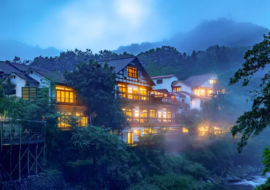 Exterior view of large, white building with illuminated lights and fog outdoors