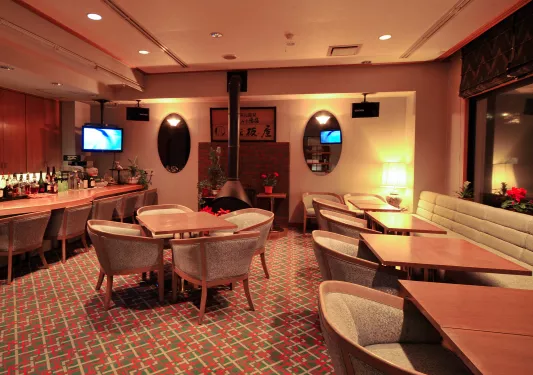 Bar and lounge with square dining tables and cushioned chairs, with a fireplace in the back