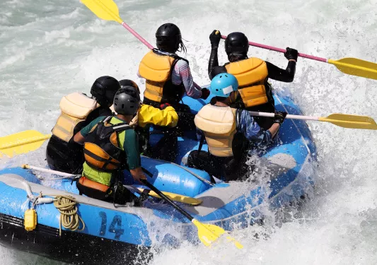 Group of people paddling on a blue raft in the middle of a river