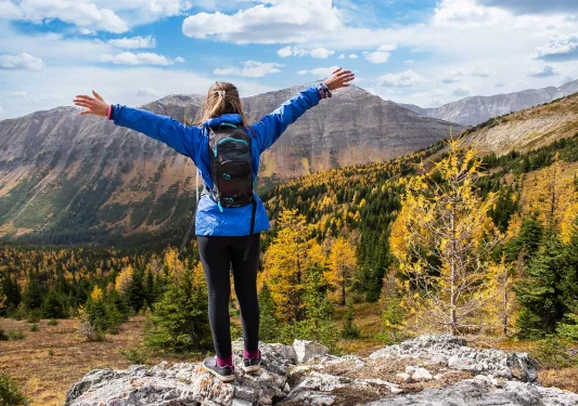 Woman wearing a blue jacket on top of a cliff with her arms wide open