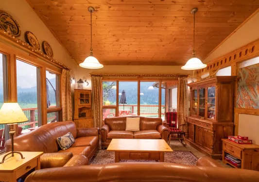 Wooden cabin room with leather couches and wooden furniture, with large windows along the walls