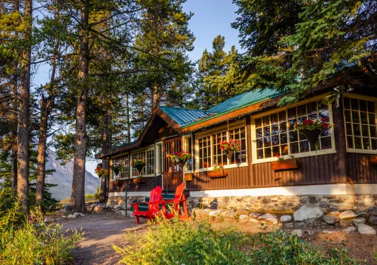 Exterior view of cabin building with two red chairs in front and large trees in the background